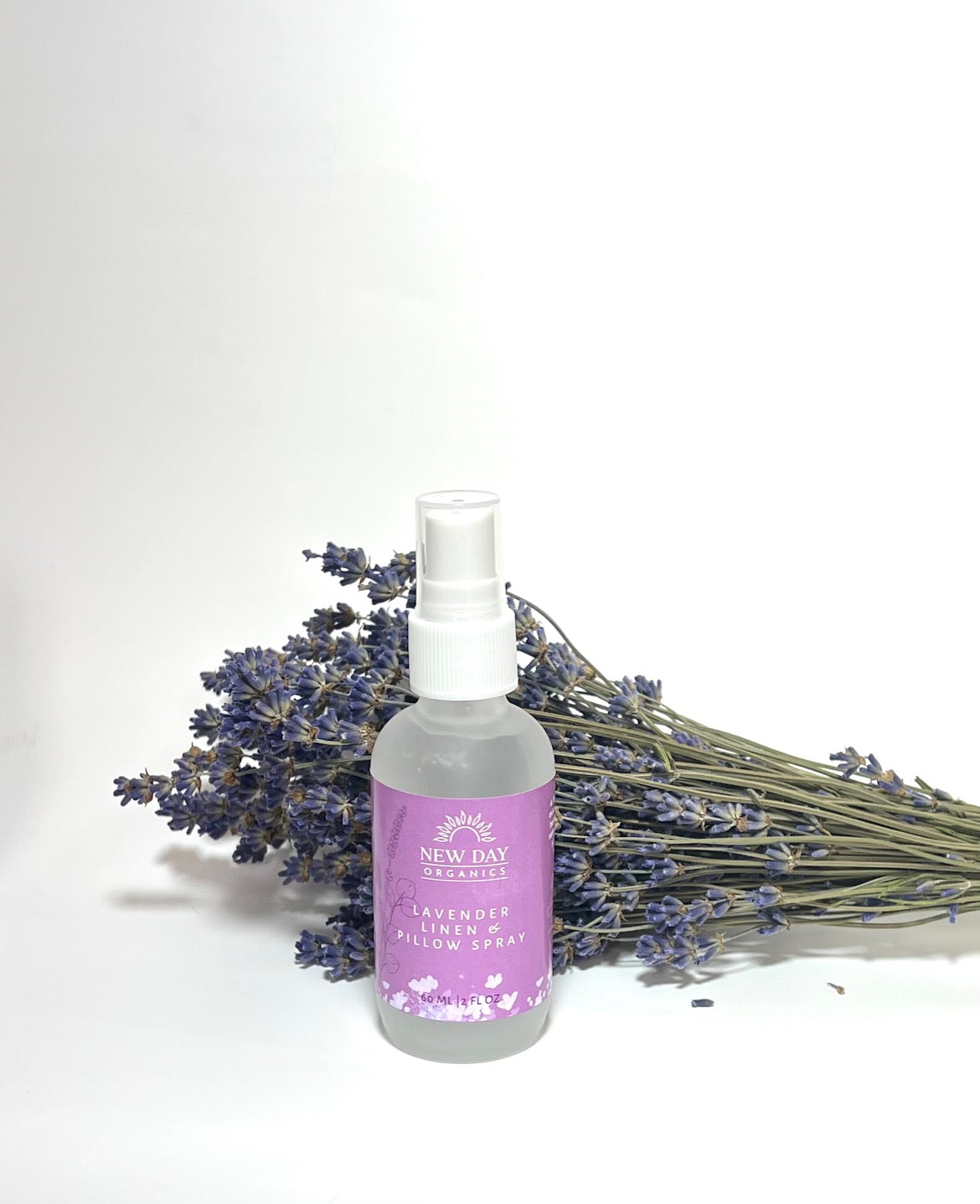 bottle of lavender linen spray in frosted glass with purple label and in front of a bunc of lavender on a white background