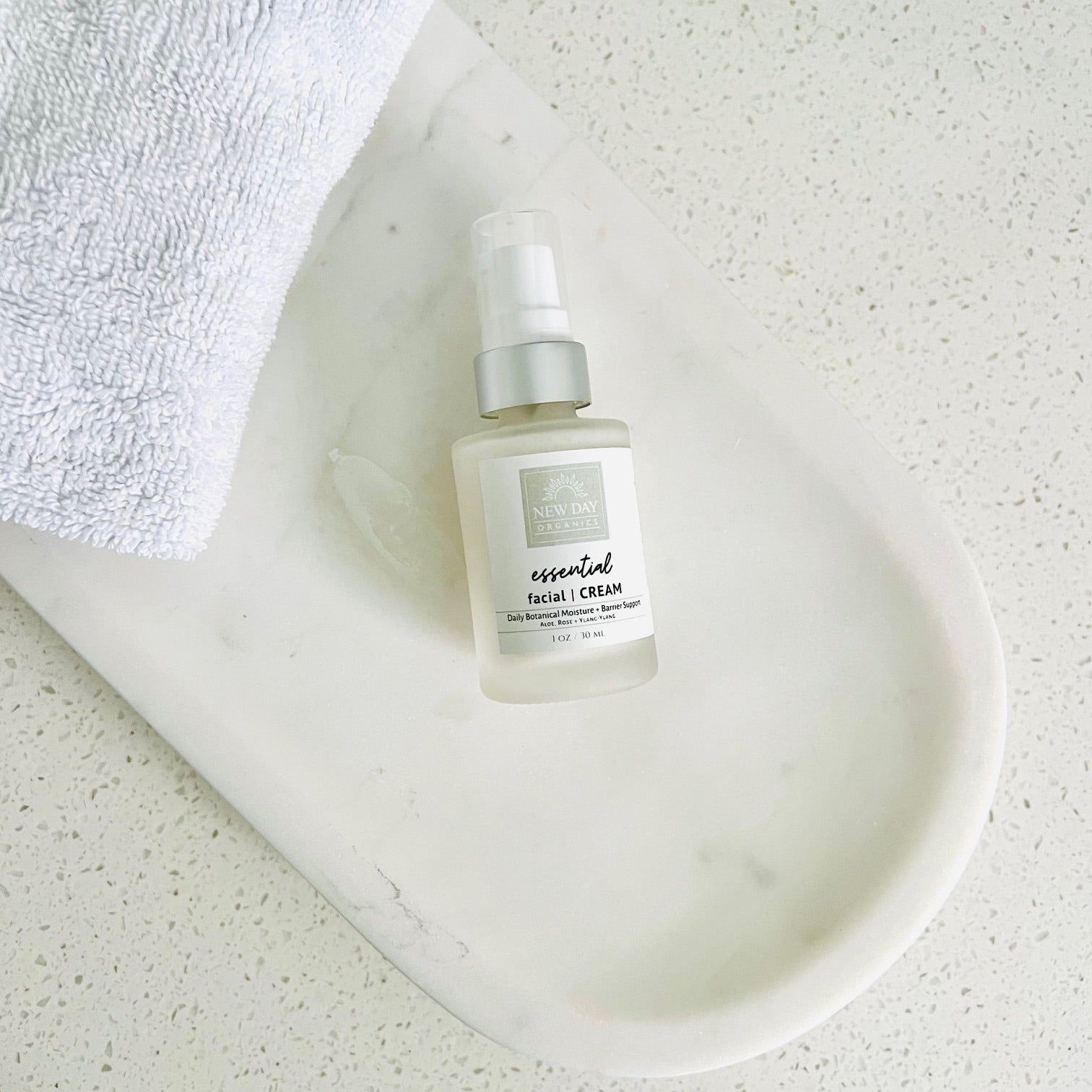 Skincare bottle labeled 'essential' on a marble surface with a white towel.