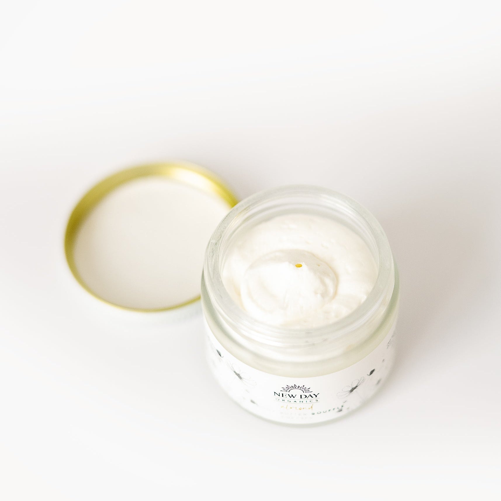 View of an open jar of Whipped Shea Body Butter Souffle with a lid on a white background