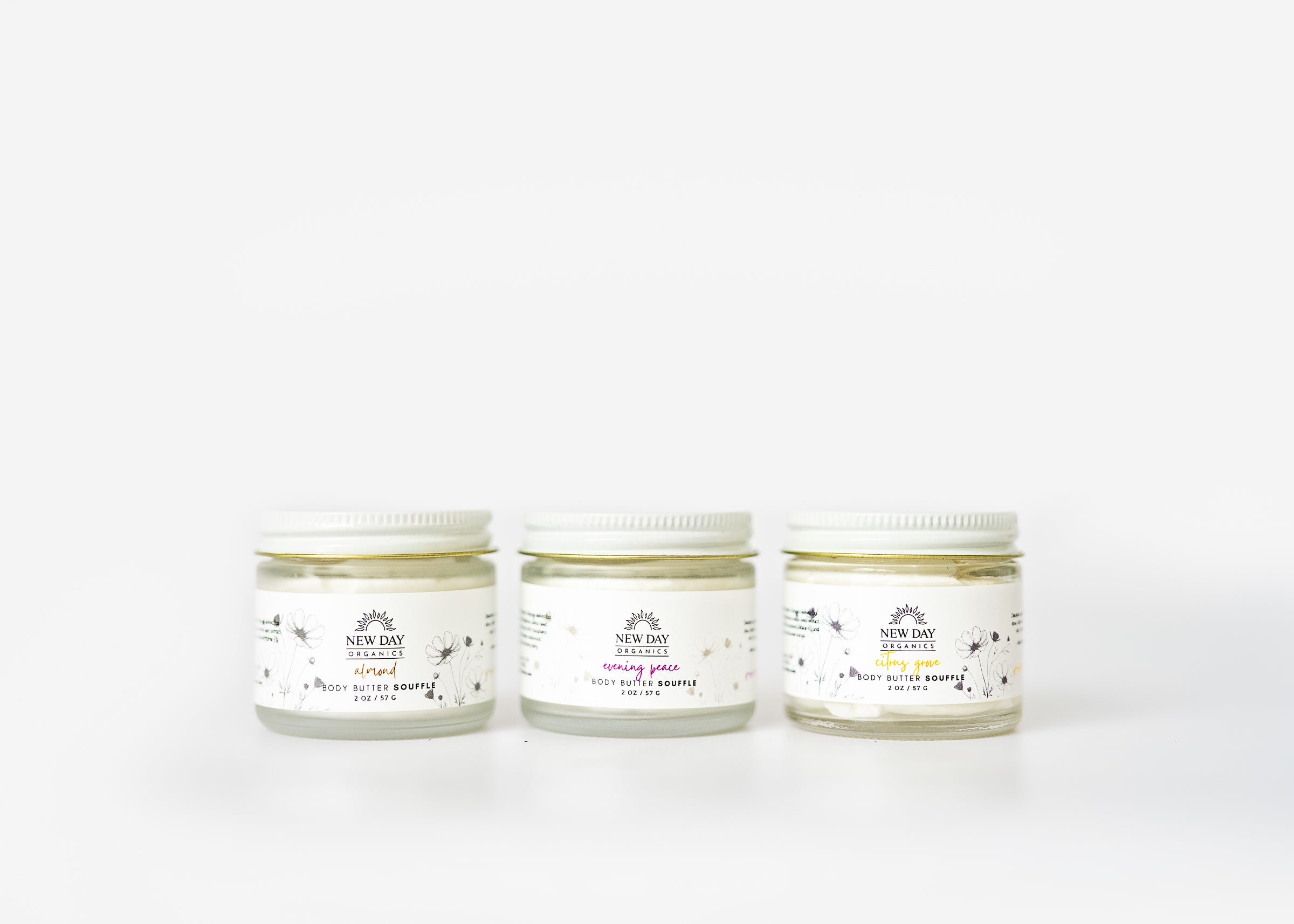 Three jars of New Day Organics body butter souffle cream on a white background