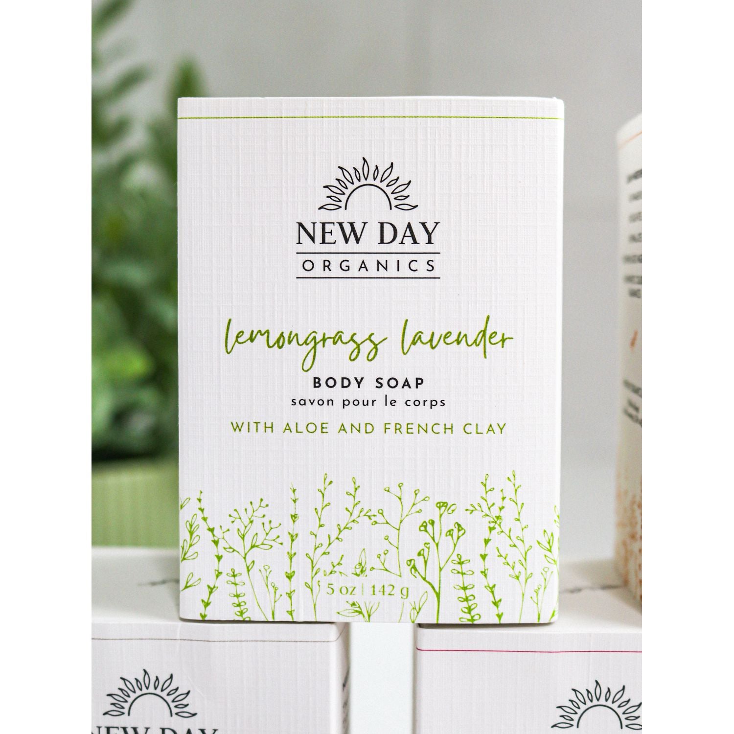 New Day Organics lemongrass lavender body soap packaging on a white surface with a blurred green plant in the background.
