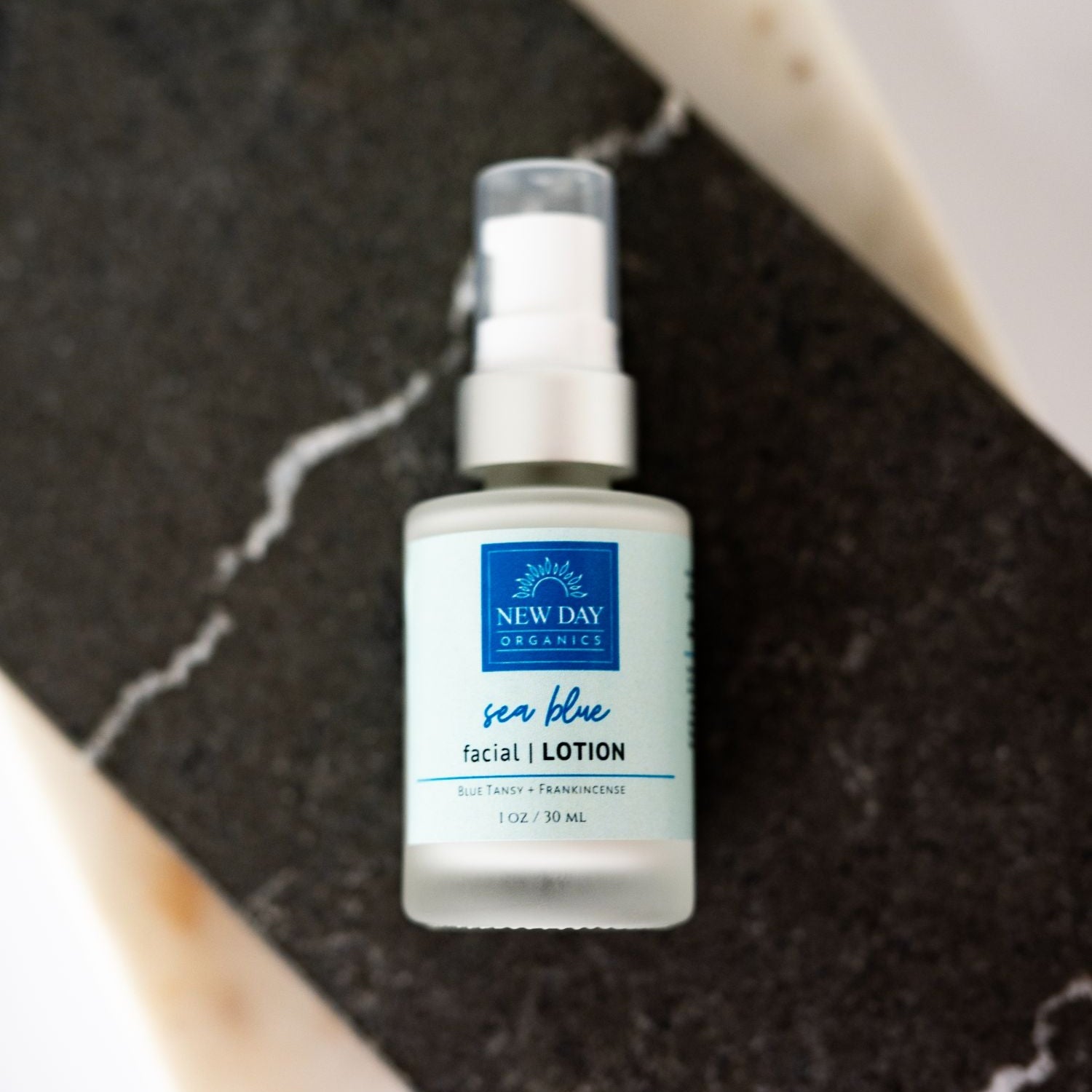 Bottle of New Day Beauty sea blue facial lotion on a dark textured surface
