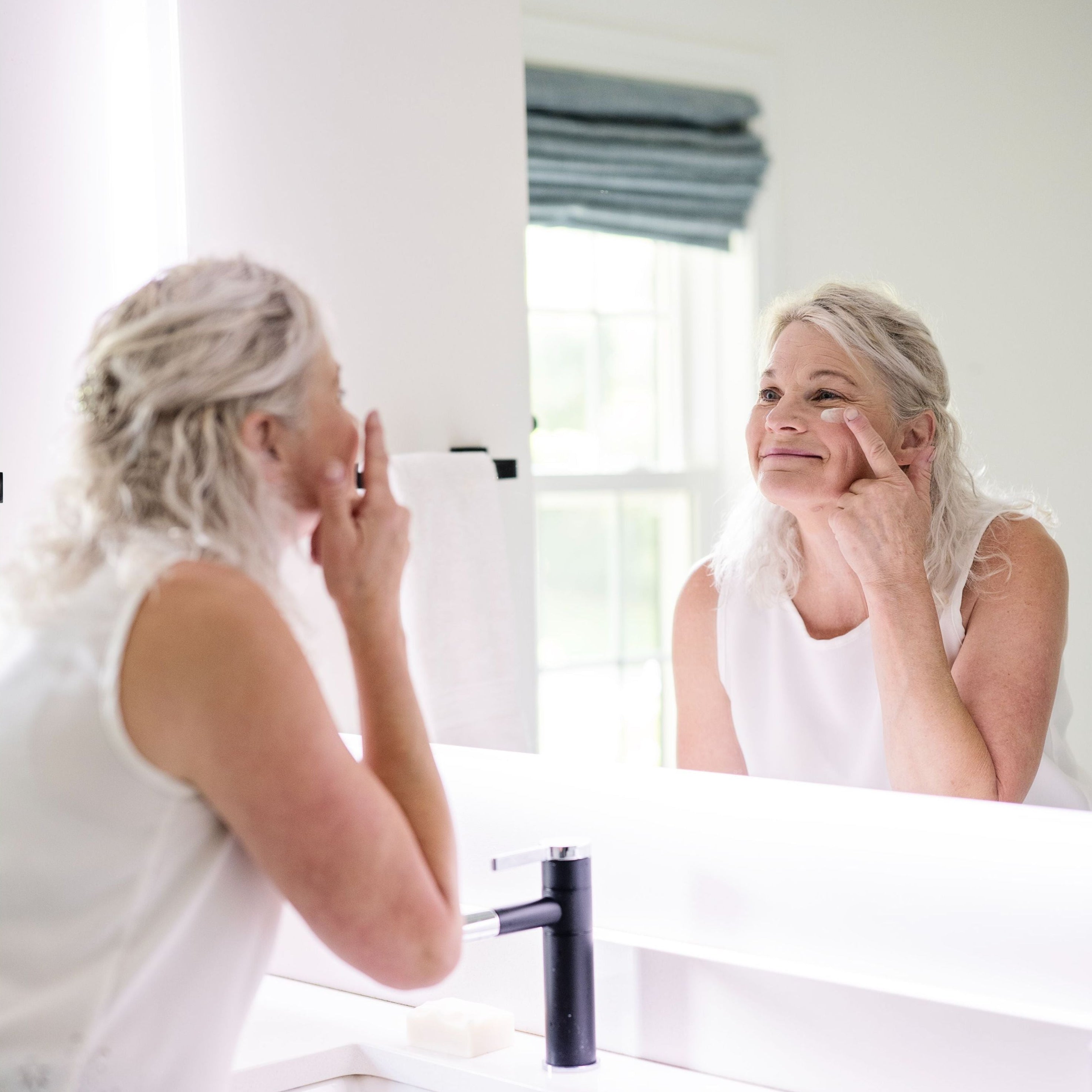 Woman applying skincare product in front of a mirror