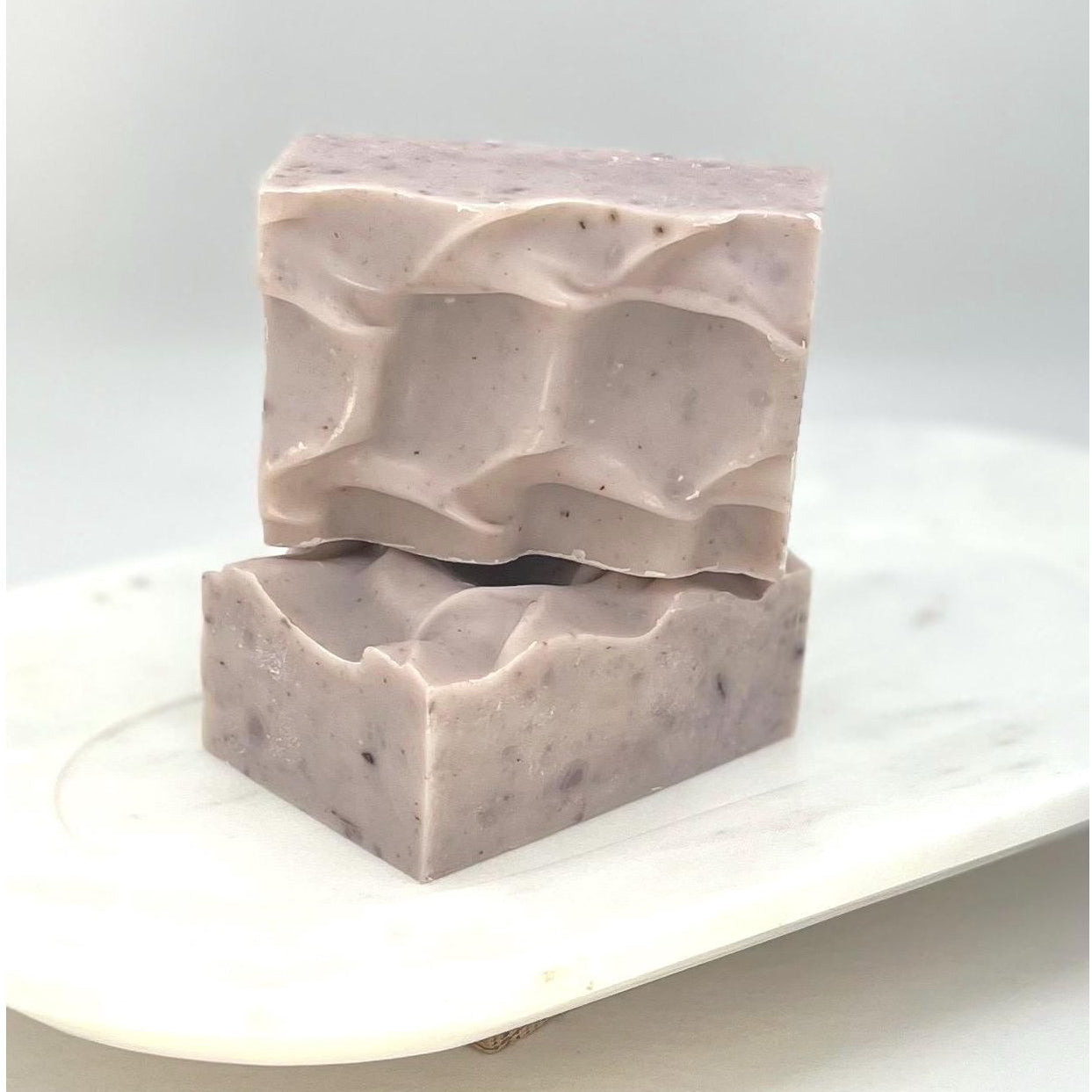 Two bars of Lavender Pine soap stacked on a white marble surface with a light gray background