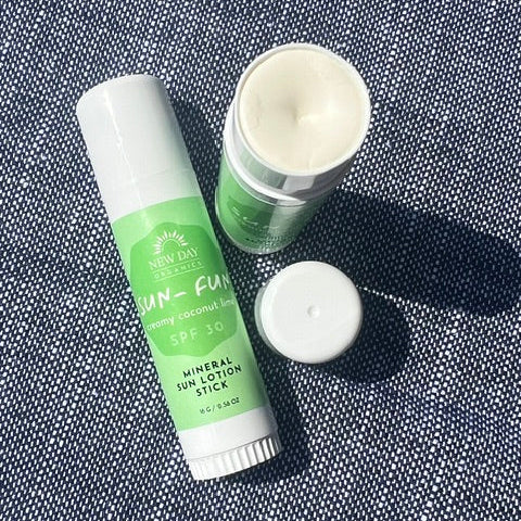 A tube of Sunny Day Skincare 'Sun-Fun' SPF 50 mineral sun lotion stick lies on a textured blue denim background next to an open jar showing the white lotion inside and a detached white cap.