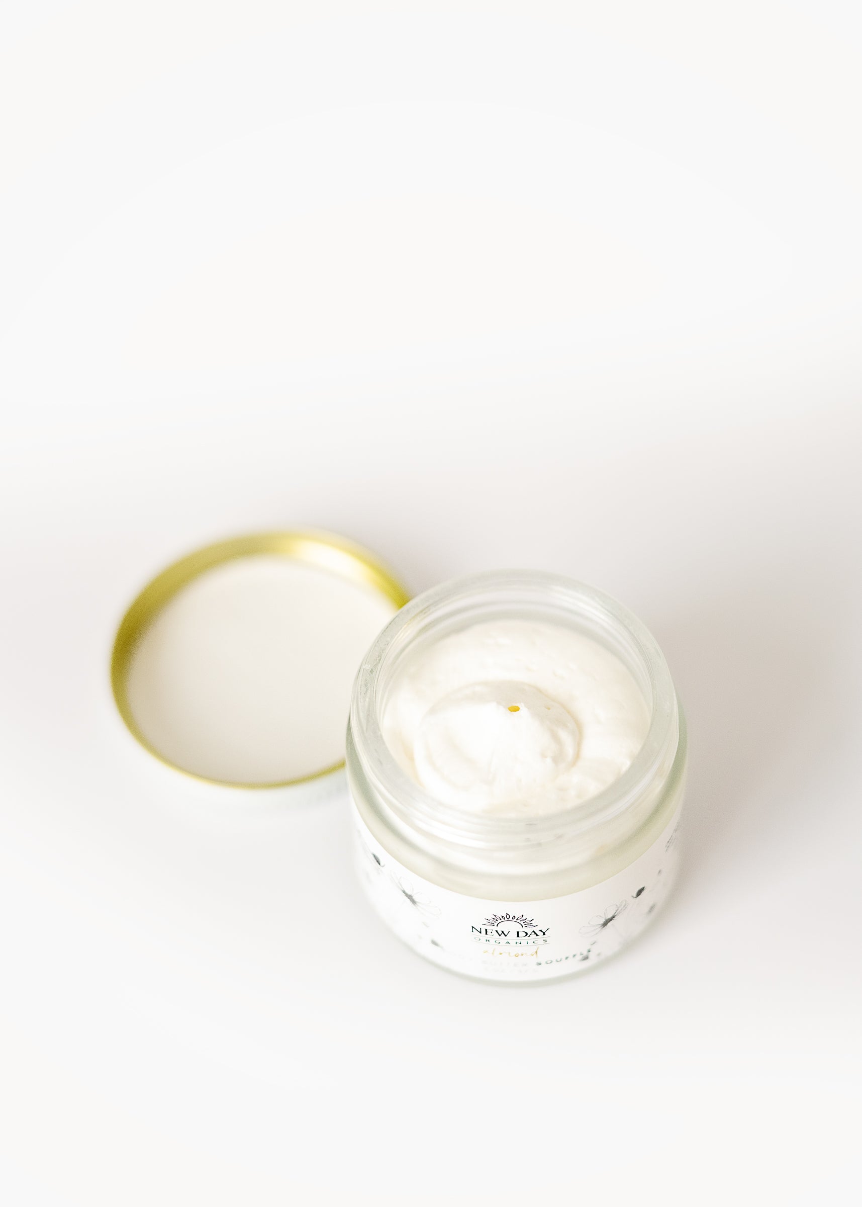 View of an open jar of Whipped Shea Body Butter Souffle with a lid on a white background