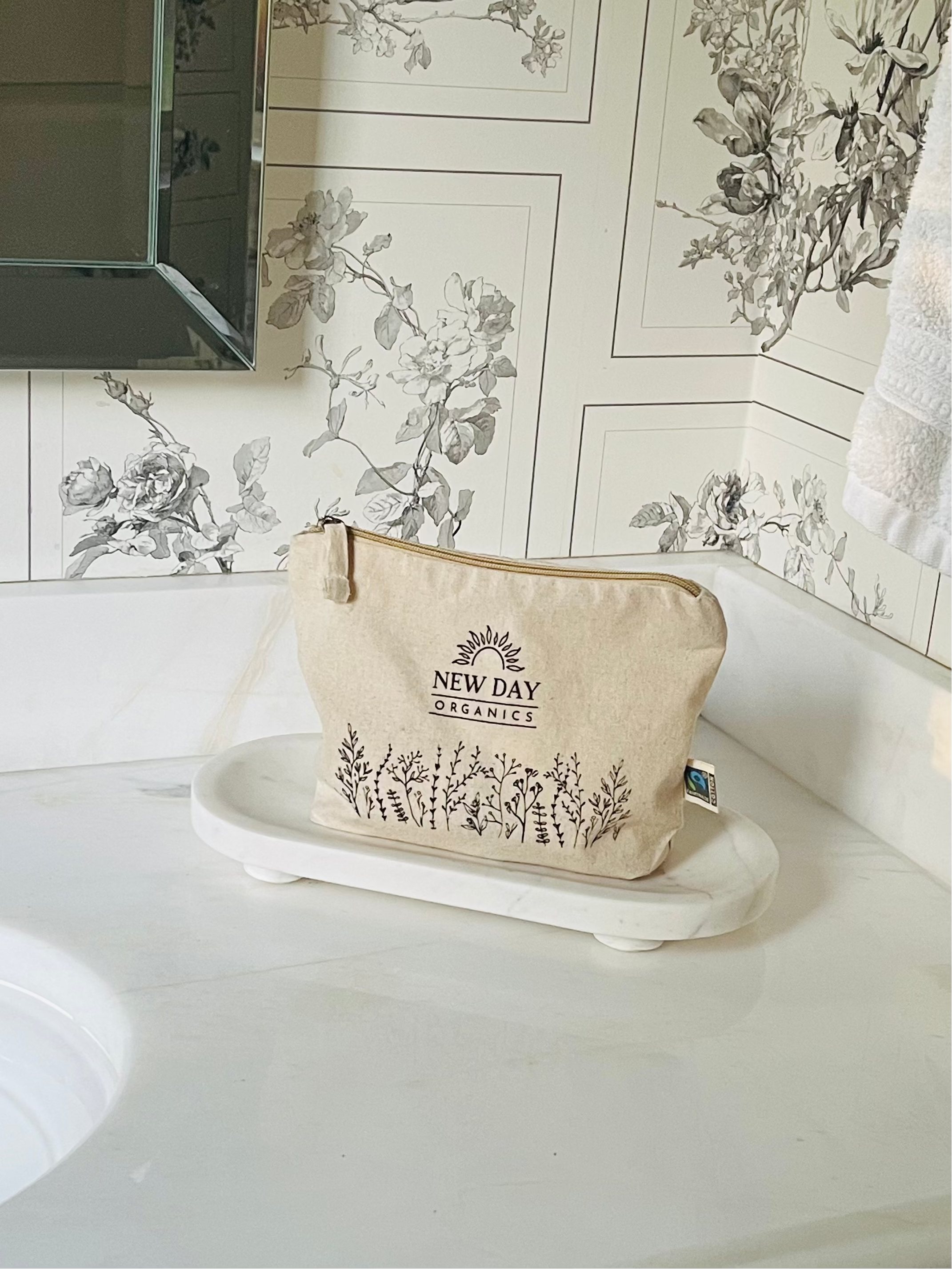 New Day Organics zippered gift pouch on a bathroom counter with floral wallpaper