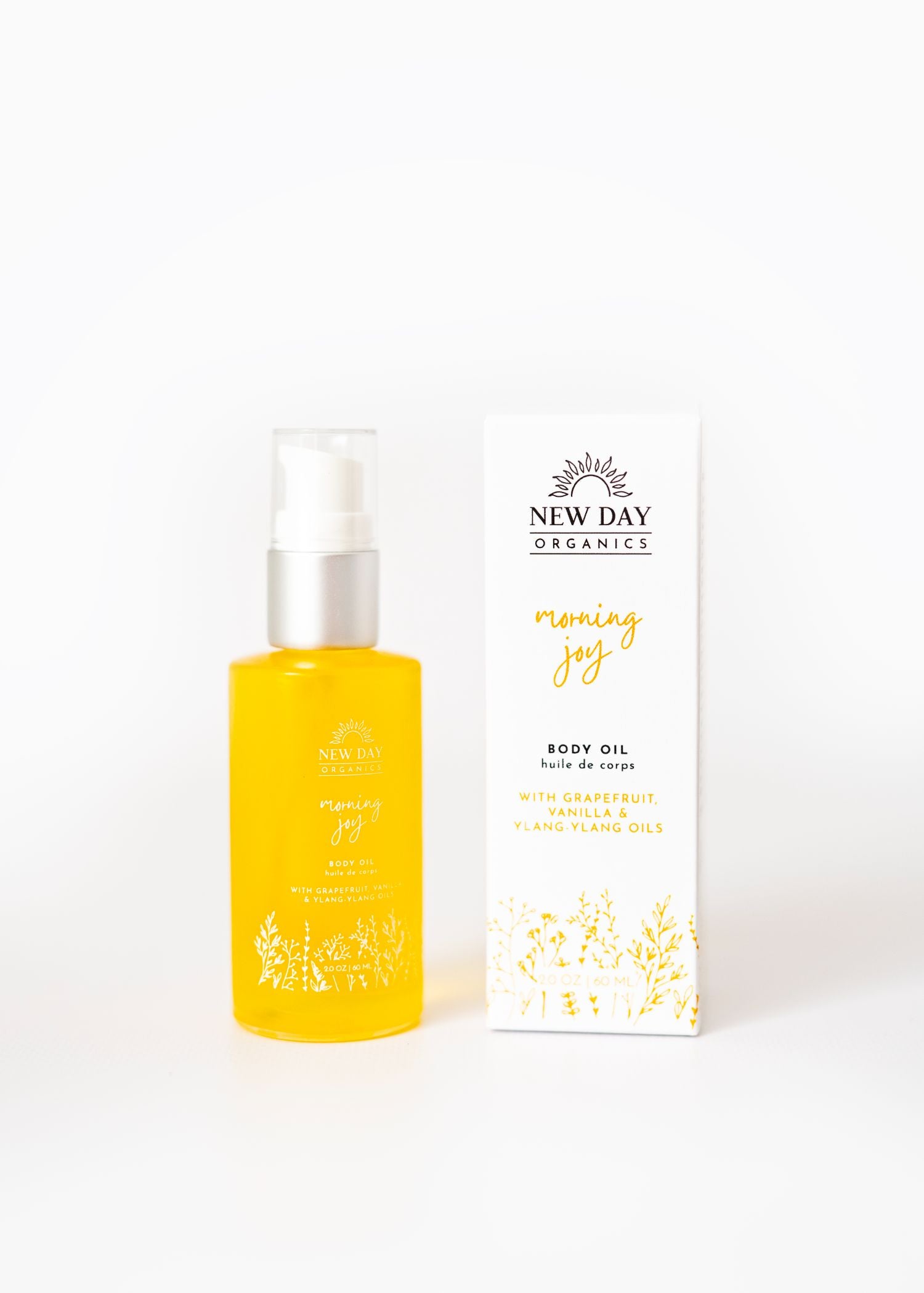 Yellow bottle and white box of New Day Organics Morning Joy body oil on a white background