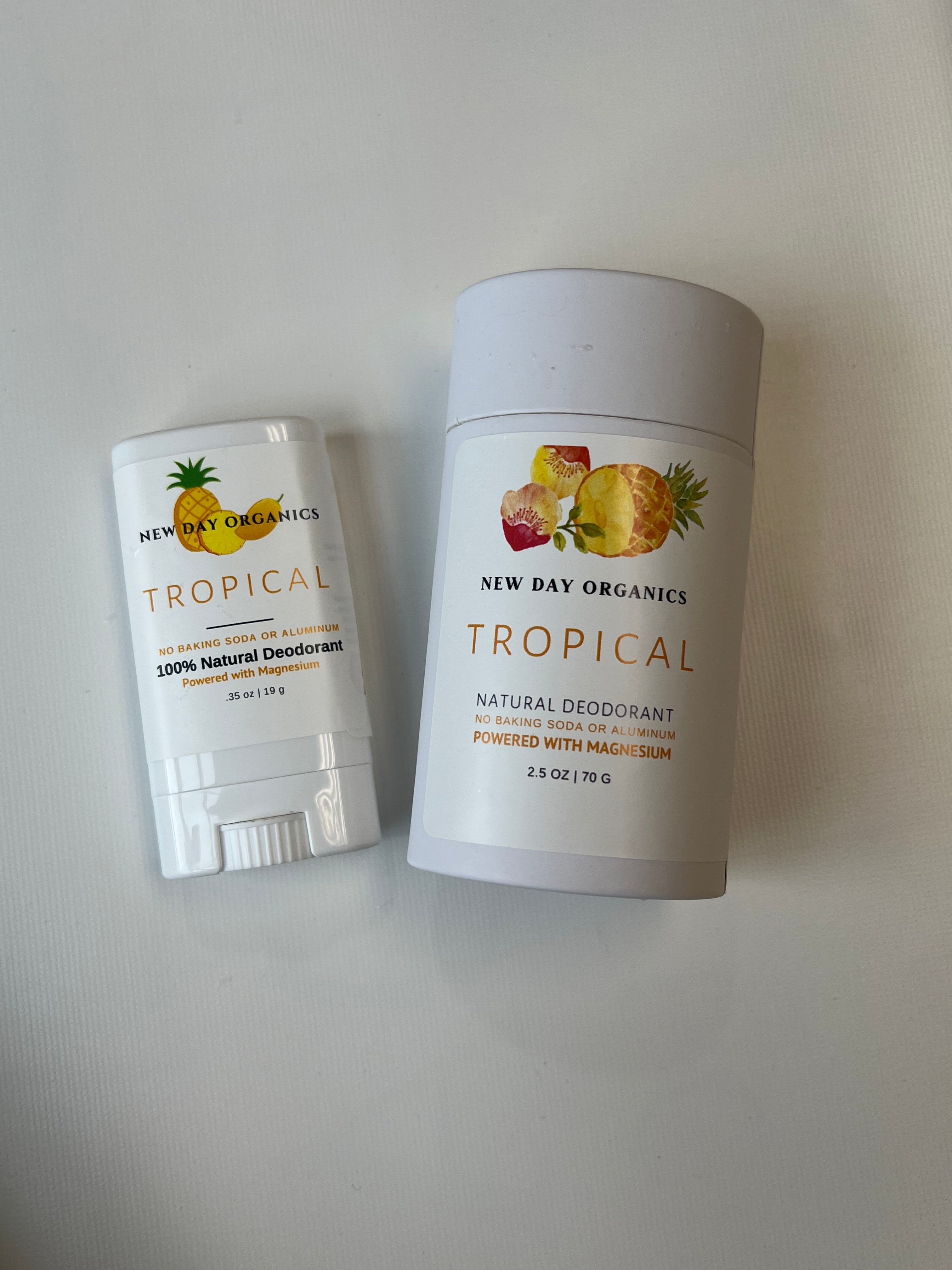 Two containers of New Day Organics Tropical deodorant on a light gray background