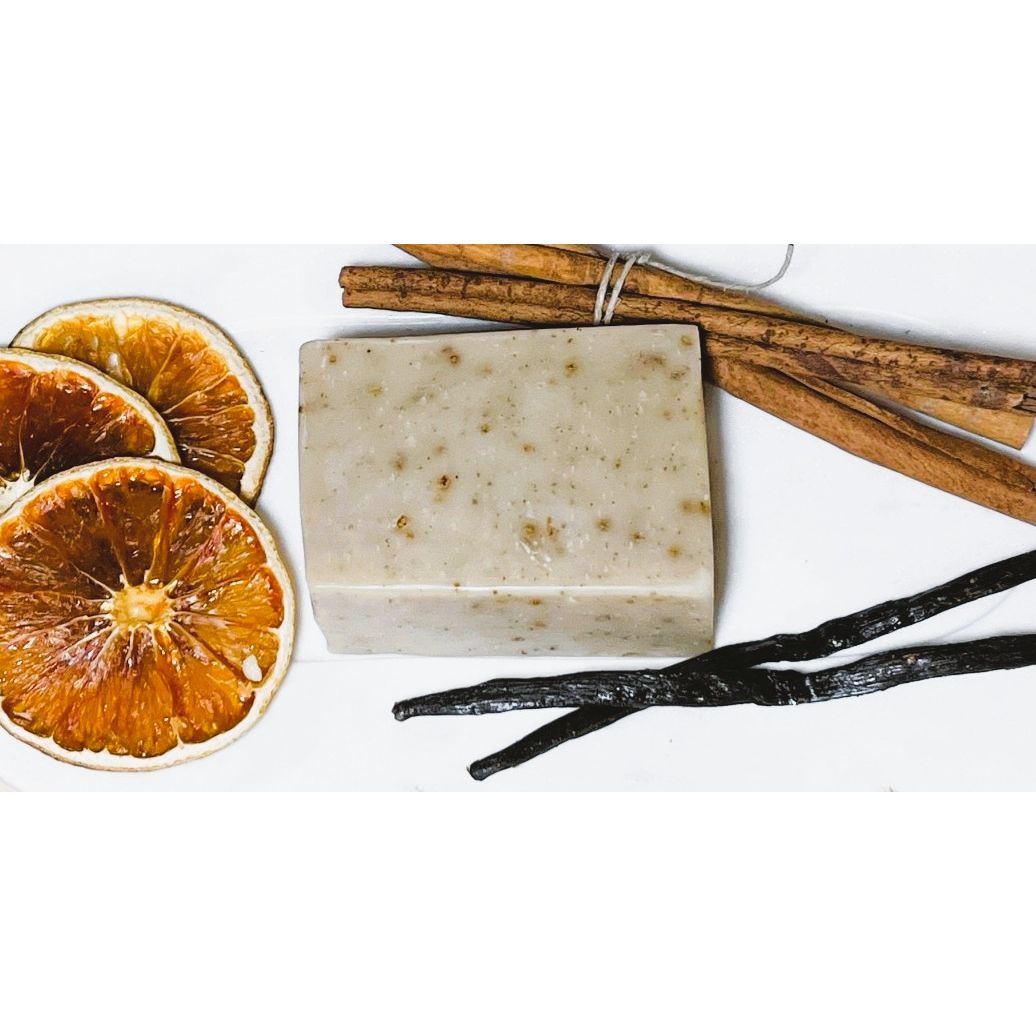Bar of soap with vanilla beans, cinnamon sticks, and dried oranges on a white background