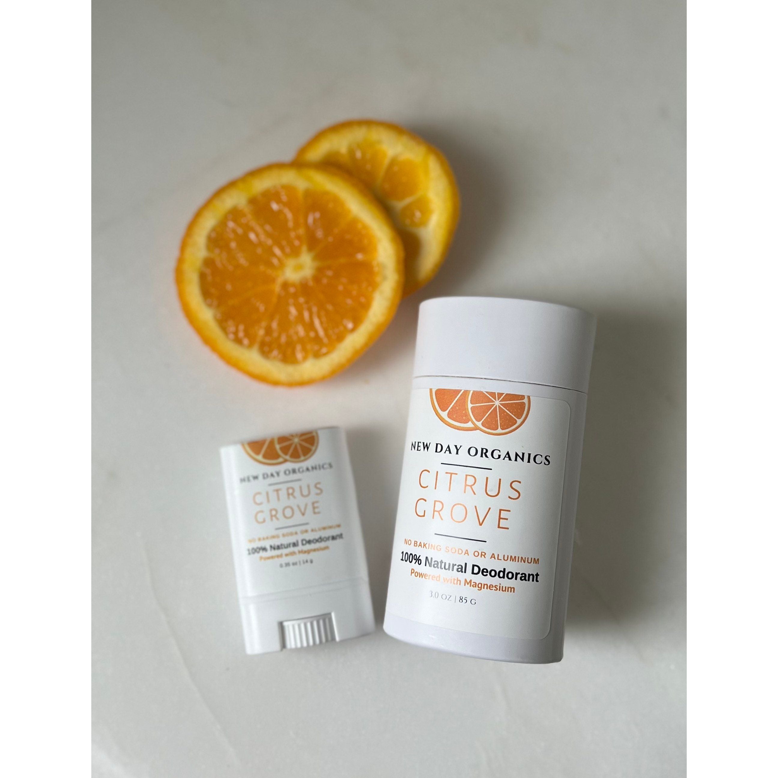 Two natural deodorant sticks with a sliced orange on a light background