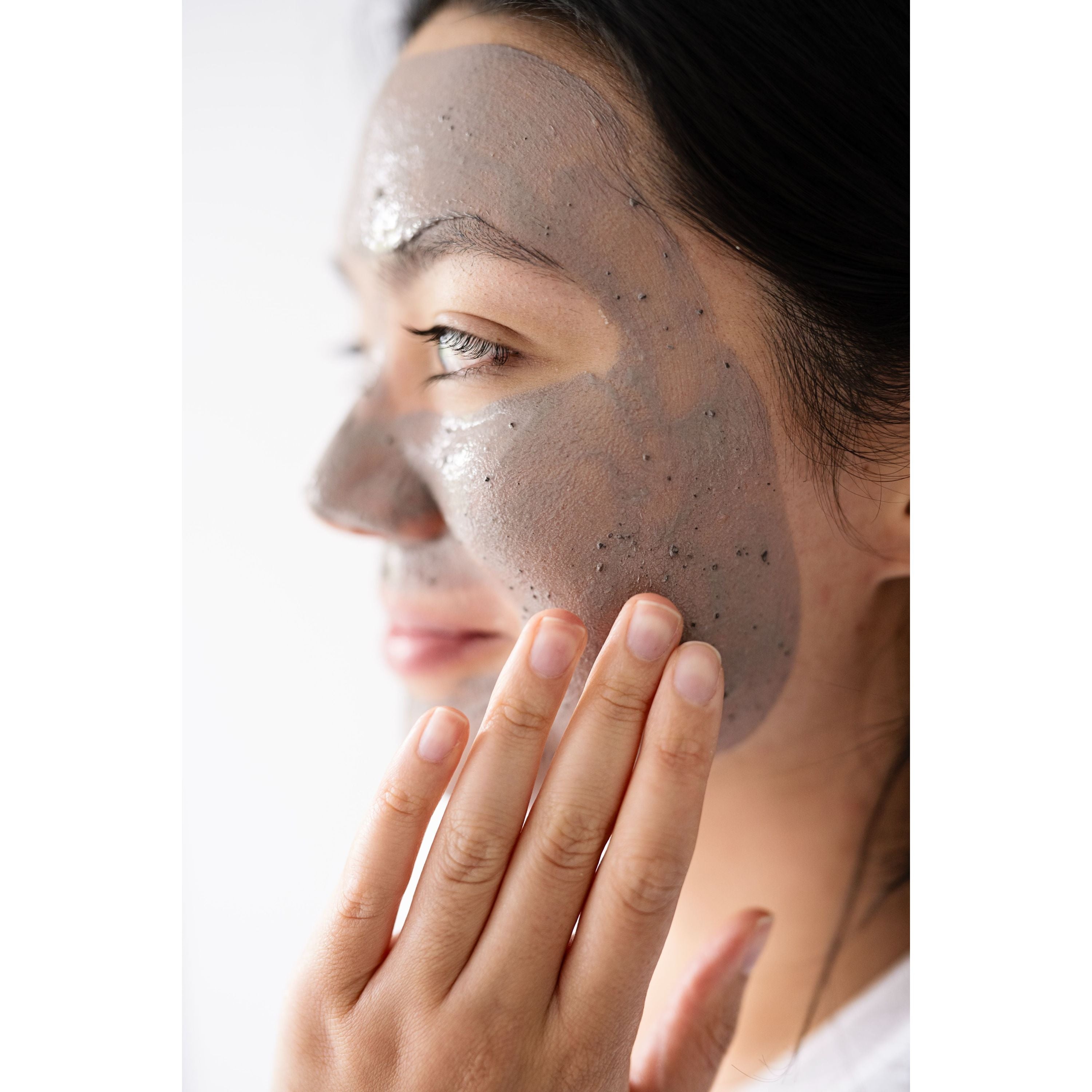 Woman applying a facial mask with a neutral background
