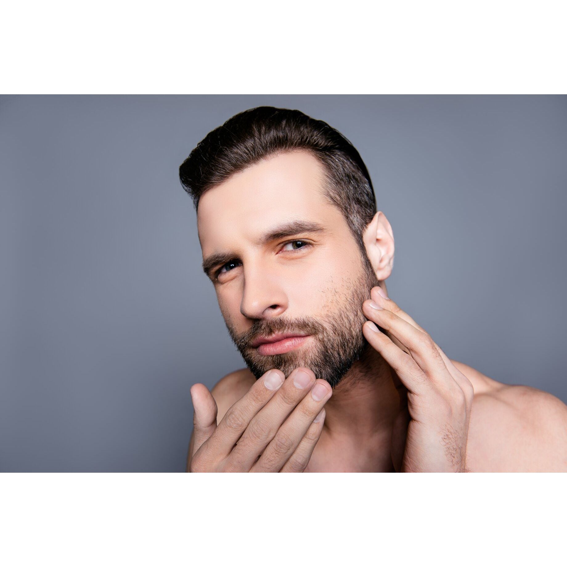 Man with a beard touching his face against a gray background
